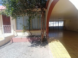 Un edificio con un espacio exterior techado, un pequeño árbol y suelo de baldosas.