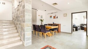 Un interior moderno con una escalera de piedra, un comedor con mesa y sillas de madera y un espacio de sala de estar con un sofá y una mesa de centro.