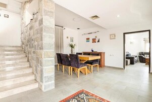 A modern interior with a stone staircase, a dining area with a wooden table and chairs, and a living space with a sofa and a coffee table.