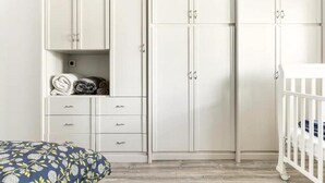 Una habitación con un armario blanco, una cuna y una cama con un cojín estampado.