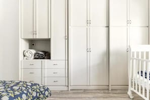 Ein Zimmer mit einem weiĂen Kleiderschrank, einem Babybett und einem Bett mit einem gemusterten Kopfkissen.
