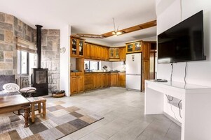 A kitchen with wooden cabinets, a built-in stove, a refrigerator, and a flat-screen TV mounted on the wall.