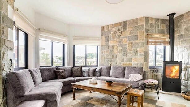 Una sala de estar moderna con una pared de piedra, un sofá seccional grande, una mesa de centro de madera y una chimenea.