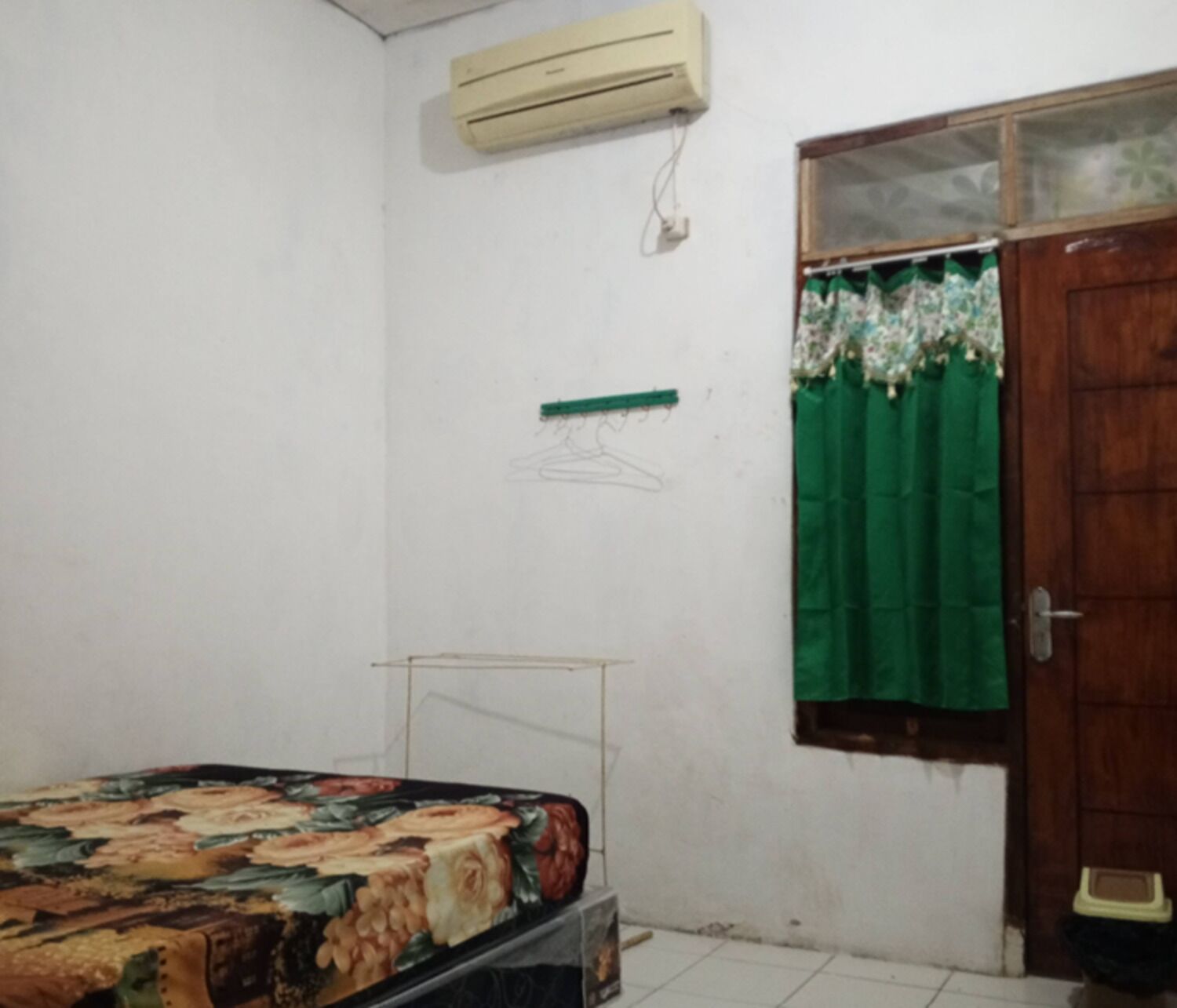 A bedroom with a bed, an air conditioner, a window with a curtain, and a door.