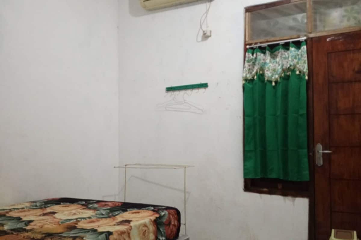 A bedroom with a bed, an air conditioner, a window with a curtain, and a door.