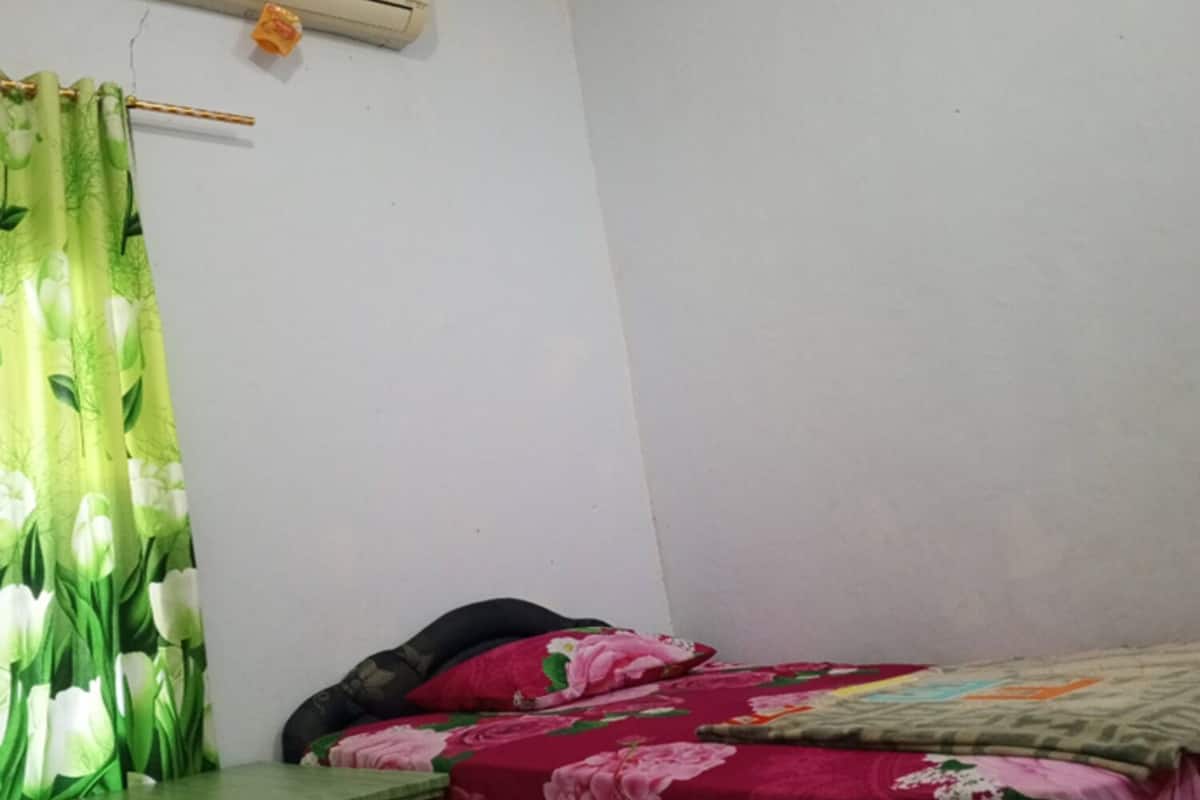 A bedroom with a bed, a table, a curtain, and an air conditioner.