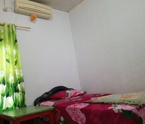 A bedroom with a bed, a table, a curtain, and an air conditioner.