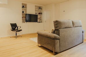 Una sala de estar moderna con un sofá gris, una silla de oficina negra, un televisor de pantalla plana montado en una pared blanca y suelo de madera.