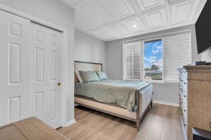 Une chambre à coucher avec un lit, une commode, une porte et une fenêtre avec des stores.