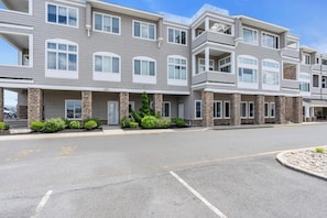 A multi-story residential building with a stone facade, multiple balconies, and a parking lot.
