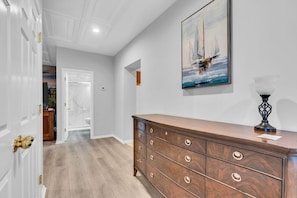 A hallway with a wooden dresser, a painting of sailboats, and a lamp.