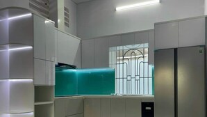 A modern kitchen with built-in appliances, a window with a metal grid, and a corner refrigerator. - 3-bedroom house in welcoming Thanh Dien with AC comfort (Thanh Dien)