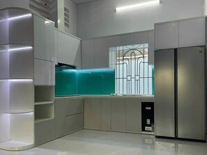 A modern kitchen with built-in appliances, a window with a metal grid, and a corner refrigerator. - 3-bedroom house in welcoming Thanh Dien with AC comfort (Thanh Dien)