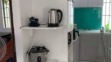 A kitchen with white cabinets, a kettle, a rice cooker, and a fan.
