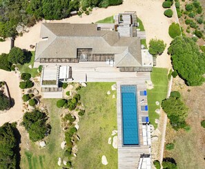 Ein weiter Blick von oben auf ein großes Haus mit Schwimmbecken, umgeben von angelegten Gärten und einem Sandbereich.