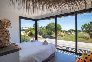 Ein Schlafzimmer mit einem großen Bett, Blick ins Freie und einem Strohdach.