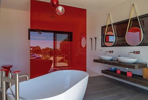 Une salle de bain moderne avec une baignoire sur pieds, un grand miroir et une fenêtre donnant sur un jardin.