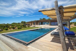 Ein moderner Poolbereich mit Holzterrasse, Liegestühlen und einer überdachten Sitzecke.