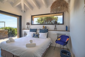 Une chambre à coucher avec un lit, des oreillers, une chaise, une fenêtre et une vue sur la verdure.
