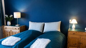 A double bed with teal bedding, two white towels, a wooden nightstand with a lamp, and a wooden dresser. - 4 Star Holiday Home in Grenaa (Grenaa)