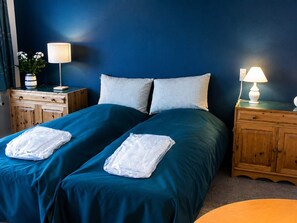A double bed with teal bedding, two white towels, a wooden nightstand with a lamp, and a wooden dresser. - 4 Star Holiday Home in Grenaa (Grenaa)