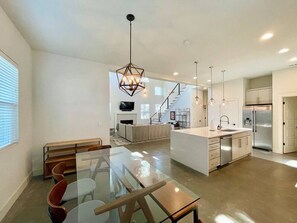 A modern kitchen with a central island, a dining area with a glass table, and a staircase leading to an upper level.