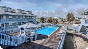 Un área de piscina con un pabellón, una terraza de madera y vistas de edificios cercanos.