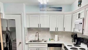 Una cocina con armarios blancos, un refrigerador de acero inoxidable, un lavavajillas y una estufa.