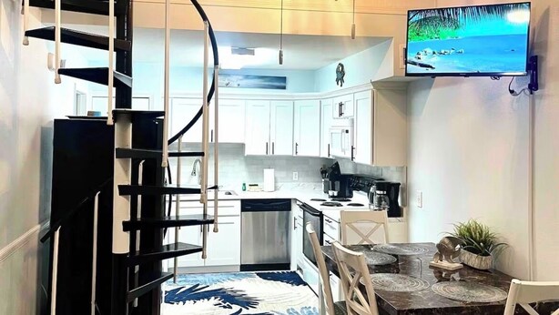 Una cocina moderna con armarios blancos, un comedor con mesa y sillas de madera, y una escalera en espiral.