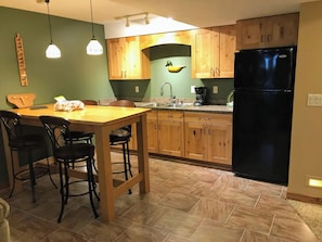 Eine Küche mit Holzausstattung, einem schwarzen Kühlschrank, einem Esstisch mit Stühlen und Pendelleuchten.