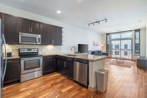 A modern kitchen with dark cabinets, stainless steel appliances, and a large window overlooking a balcony. - Urban Houston Stay 1BR • Balcony • Fast Wi-Fi  Laundry (Houston)