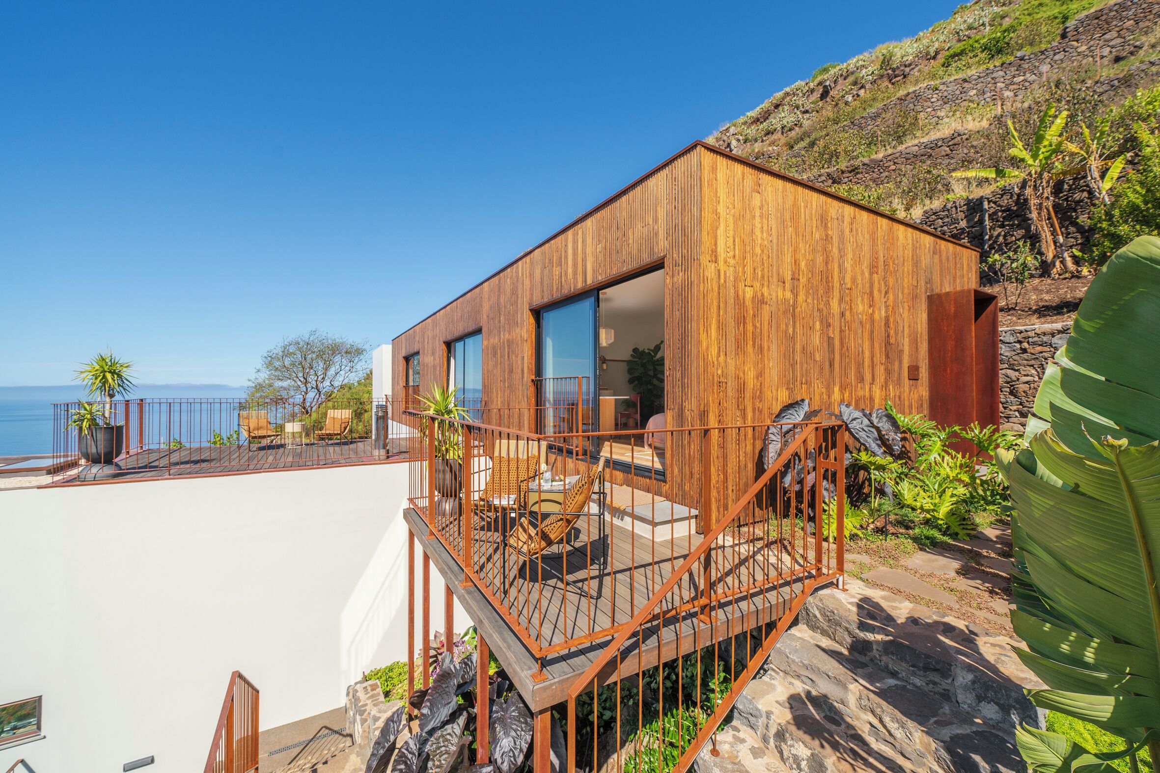 Een modern houten huis met balkon, grote ramen en uitzicht op zee.