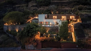 Una casa moderna con piscina, rodeada de vegetación exuberante y colinas escalonadas.