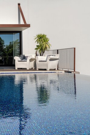 Un área de piscina moderna con dos sillones blancos y una planta en maceta.