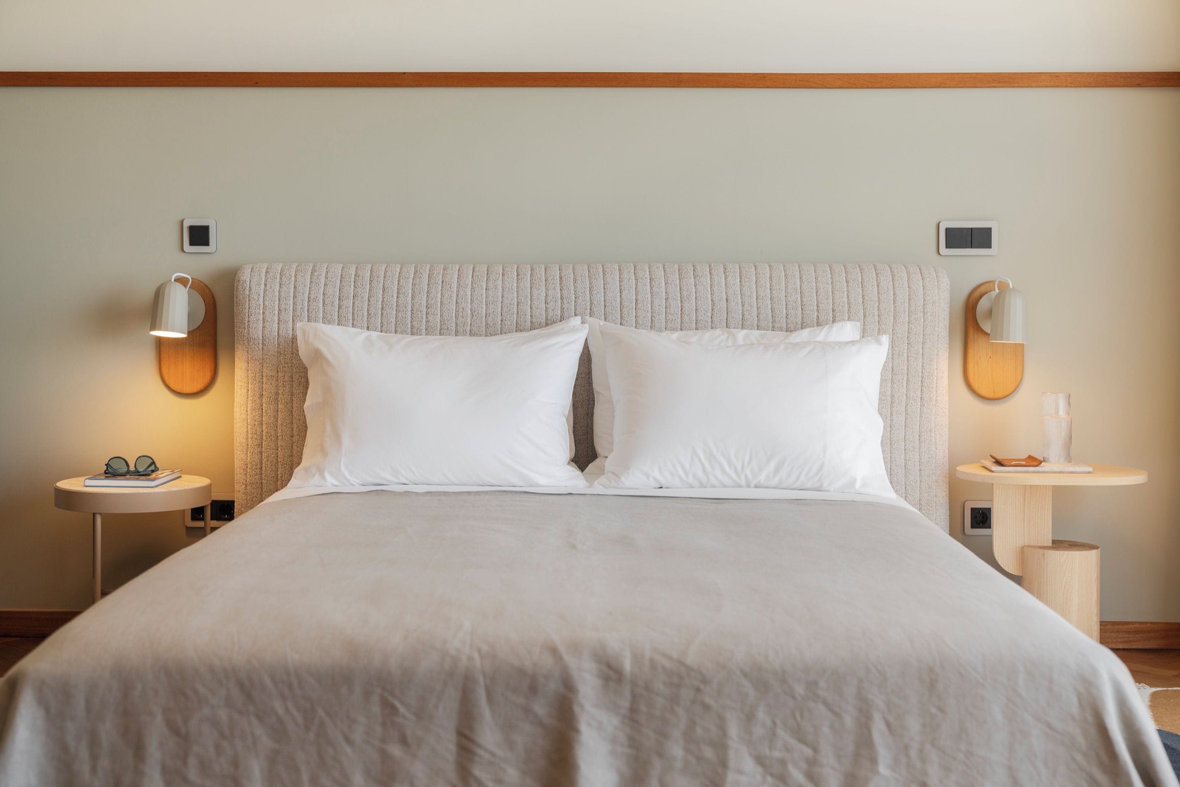 A neatly made bed with a textured headboard, two bedside tables with lamps, and a small round table with a lamp and a book.