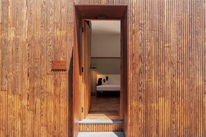 A wooden door leading to a room with a bed and a white wall. - BOTÂNICA LIVING (Camara de Lobos)