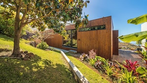 Un edificio moderno con fachada de madera, un espacio verde con un árbol y un jardín con diversas plantas.