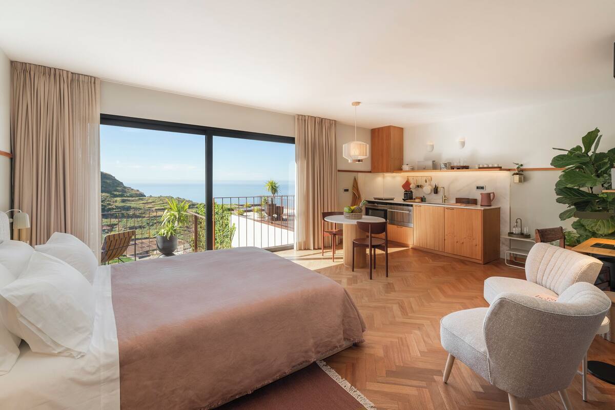 A modern hotel room with a large bed, a dining area, and a kitchen.