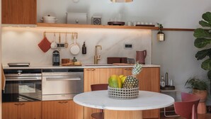 Una cocina moderna con armarios de madera, electrodomésticos de acero inoxidable, encimera de mármol y un frutero sobre una mesa.
