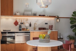 A modern kitchen with wooden cabinets, stainless steel appliances, a marble countertop, and a fruit bowl on a table.