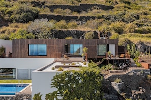 A modern house with a pool, large windows, and a stone retaining wall.