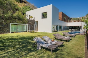 A modern house with a swimming pool, outdoor seating, and a stone wall.