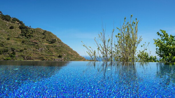 Una piscina azul y cristalina con vistas a un paisaje montañoso y árboles.