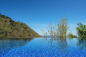 A clear blue pool with a view of a hilly landscape and trees.