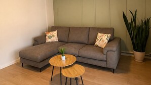 A living room with a sectional sofa, two round wooden tables, a potted plant, and a ceiling light fixture. - Villa Lucija - Old town and Lake view Apartment (Ohër)