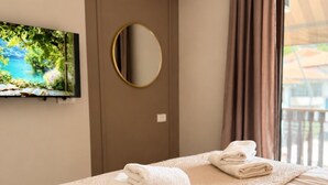 A hotel room with a bed, a round mirror, a flat-screen TV, and a window with curtains. - Villa Lucija - Old town and Lake view Apartment (Ohër)