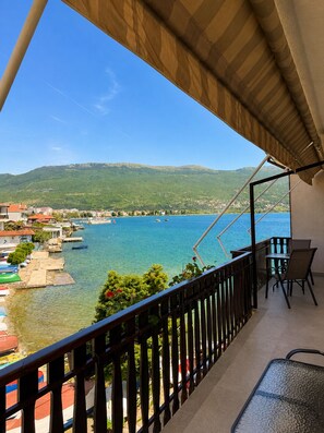Un balcón con vista a un lago, barcos y un pueblo lejano.