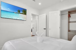 Ein Schlafzimmer mit einem Bett, einem Fernseher, der eine Strandansicht zeigt, weißen Wänden und einem Kleiderschrank.