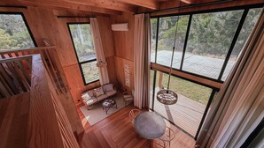 Interior em madeira com janelas amplas, um sofá, uma mesa e um lustre.