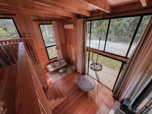 Ein Holzinnenraum mit großen Fenstern, einem Sofa, einem Tisch und einer Pendelleuchte.